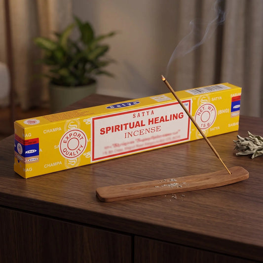 Satya Spiritual Healing Räucherstäbchen: glimmendes Räucherstäbchen mit feinem Rauch im Holzhalter, dahinter die Packung, auf einem Sideboard am Abend