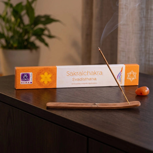 Sakralchakra Räucherstäbchen Holy Smokes: glimmendes Räucherstäbchen mit feinem Rauch im Holzhalter, dahinter die Packung, auf einem Sideboard am Abend