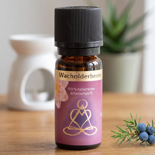 Ätherisches Öl Wacholderbeere: Fläschchen auf einem Holz-Sideboard im Wohnzimmer, im Hintergrund eine weiße Duftlampe, daneben ein Wacholderzweig mit Beeren