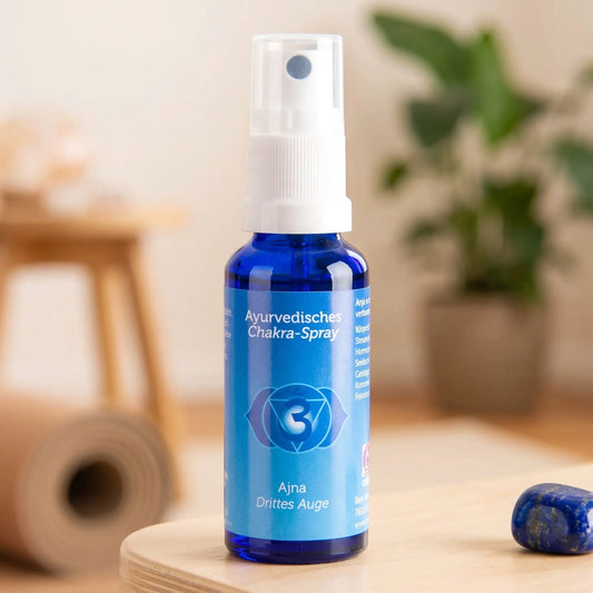 Ayurvedisches Chakra-Spray Ajna (Stirn-Chakra): 30-ml-Sprühflasche auf einem Holzhocker neben einer gerollten Yogamatte, daneben Lapislazuli