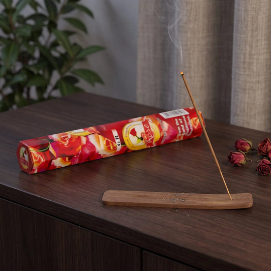 GR Rose Räucherstäbchen: glimmendes Räucherstäbchen mit feinem Rauch im Holzhalter, dahinter die Sechseck-Packung, auf einem Sideboard am Abend