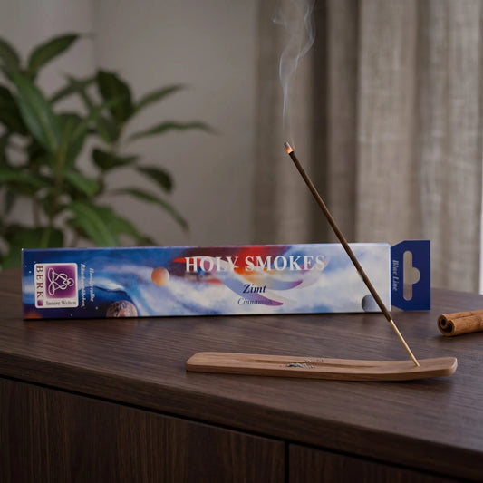 Zimt Räucherstäbchen Holy Smokes Blue Line: glimmendes Räucherstäbchen mit feinem Rauch im Holzhalter, dahinter die Packung, auf einem Sideboard am Abend