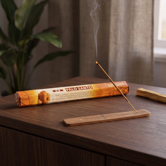 GR Palo Santo Räucherstäbchen: glimmendes Räucherstäbchen mit feinem Rauch im Holzhalter, dahinter die Sechseck-Packung, auf einem Sideboard am Abend