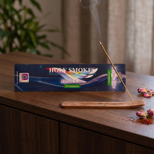 Urvertrauen Räucherstäbchen Holy Smokes Mystic Line: glimmendes Räucherstäbchen mit feinem Rauch im Holzhalter, dahinter die Packung, auf einem Sideboard am Abend