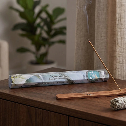 GR White Sage Räucherstäbchen: glimmendes Räucherstäbchen mit feinem Rauch im Holzhalter, dahinter die Sechseck-Packung, auf einem Sideboard am Abend