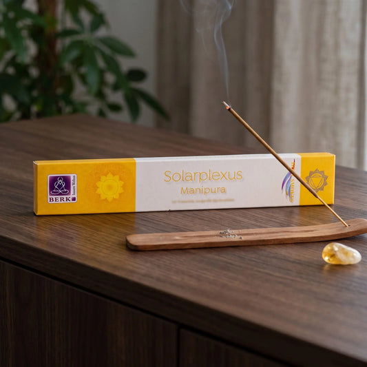 Solarplexuschakra Räucherstäbchen Holy Smokes: glimmendes Räucherstäbchen mit feinem Rauch im Holzhalter, dahinter die Packung, auf einem Sideboard am Abend