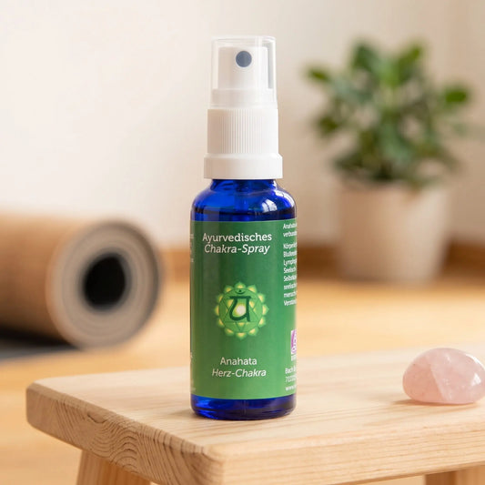 Ayurvedisches Chakra-Spray Anahata (Herz-Chakra): 30-ml-Sprühflasche auf einem Holzhocker neben einer gerollten Yogamatte, daneben Rosenquarz