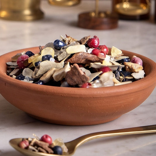 Aufbruch, Rauhnachts-Räucherung von Berk, 50 ml im Korkglas: Nahaufnahme der Terracottaschale mit rosa Pfefferbeeren, Wacholderbeeren und Harz vor der warmen, unscharfen Abendapotheke – Spirit of Gaia