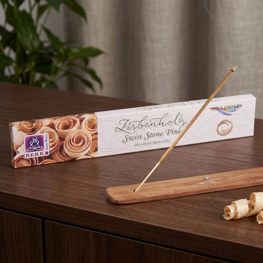 Räucherstäbchen Zirbenholz von Berk: glimmendes Räucherstäbchen mit feinem Rauch im Holzhalter, dahinter die Packung, auf einem Sideboard am Abend