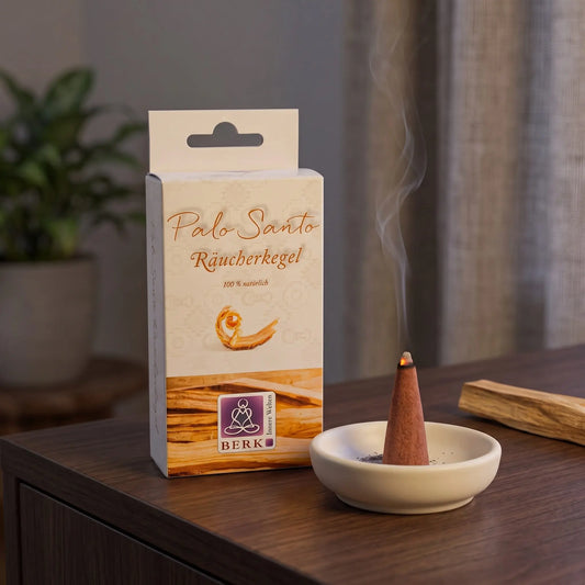 Räucherpyramiden Palo Santo von Berk: glimmender Räucherkegel mit feinem Rauch auf einem Keramiktellerchen, dahinter die Schachtel, auf einem Sideboard am Abend