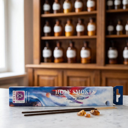 Amber Mond Räucherstäbchen Holy Smokes Blue Line: Packung auf einer Marmortheke vor einem Apothekerschrank, davor zwei lose Räucherstäbchen und Stücke goldbraunes Amberharz – Spirit of Gaia