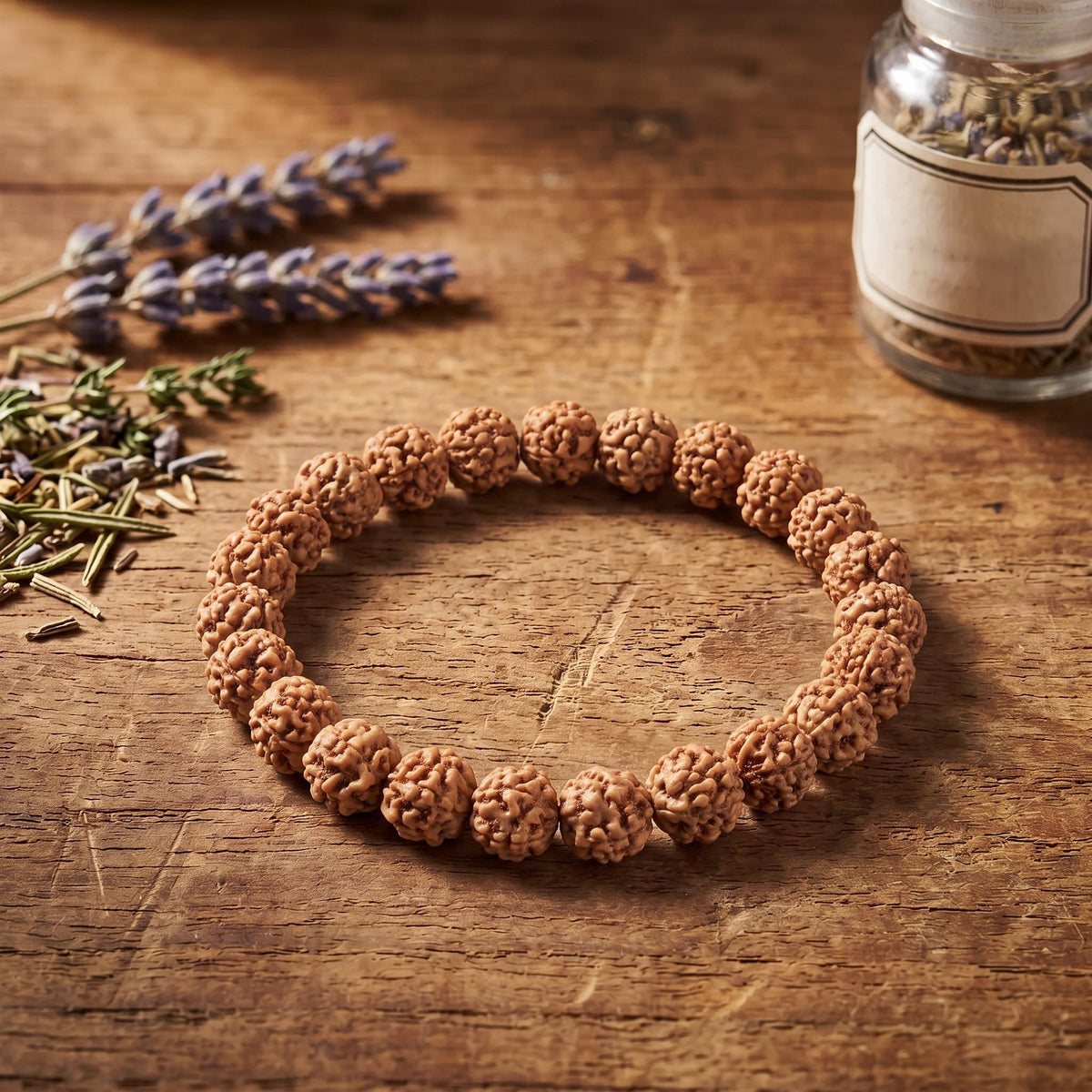 Rudraksha Armband auf einem Holztisch neben Lavendel und einem Glas mit getrockneten Kräutern