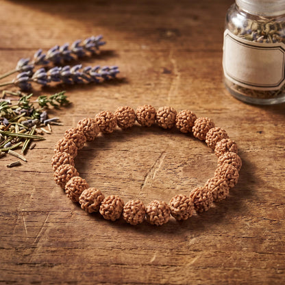 Rudraksha Armband auf einem Holztisch neben Lavendel und einem Glas mit getrockneten Kräutern