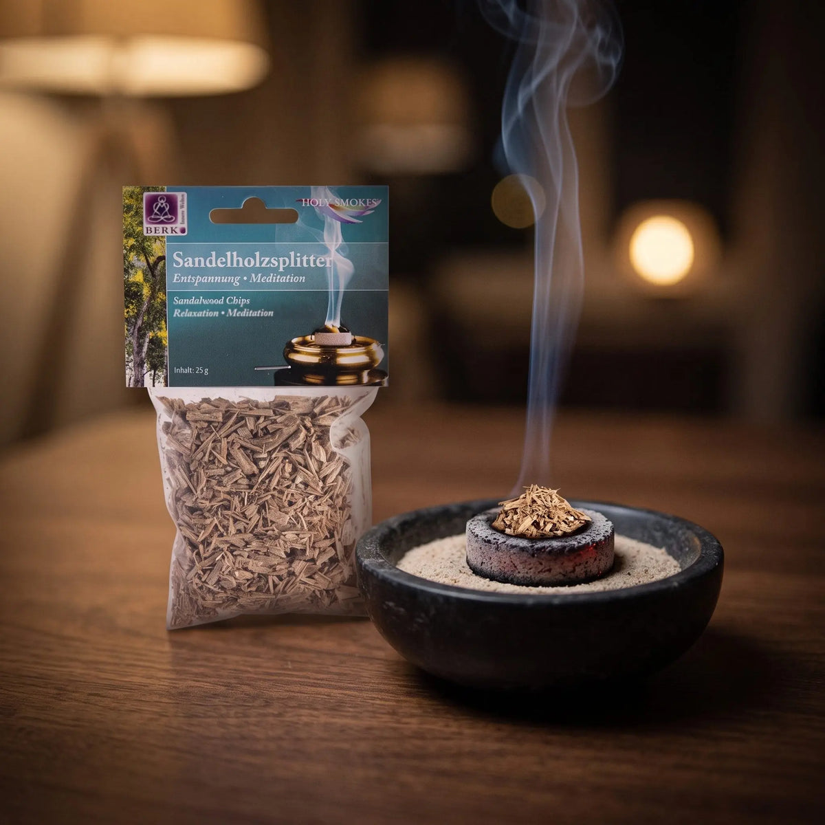 Sandelholzsplitter, sortenreines Räucherwerk von Berk, 25 g: einige Sandelholzsplitter glimmen auf der Räucherkohle, dahinter die Tüte, feiner Rauch steigt auf einer dunklen Holzplatte am Abend auf – Spirit of Gaia