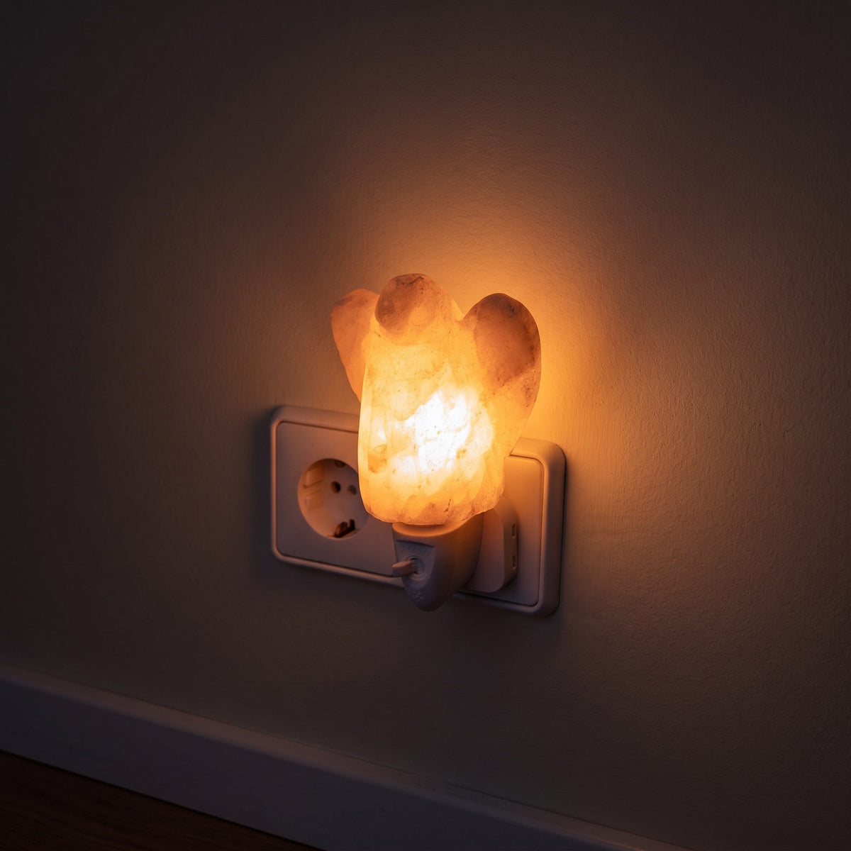 Das Salzkristall-Nachtlicht Engel in der Steckdose eines dunklen Flurs, das Licht bildet einen weichen Kreis auf der Wand