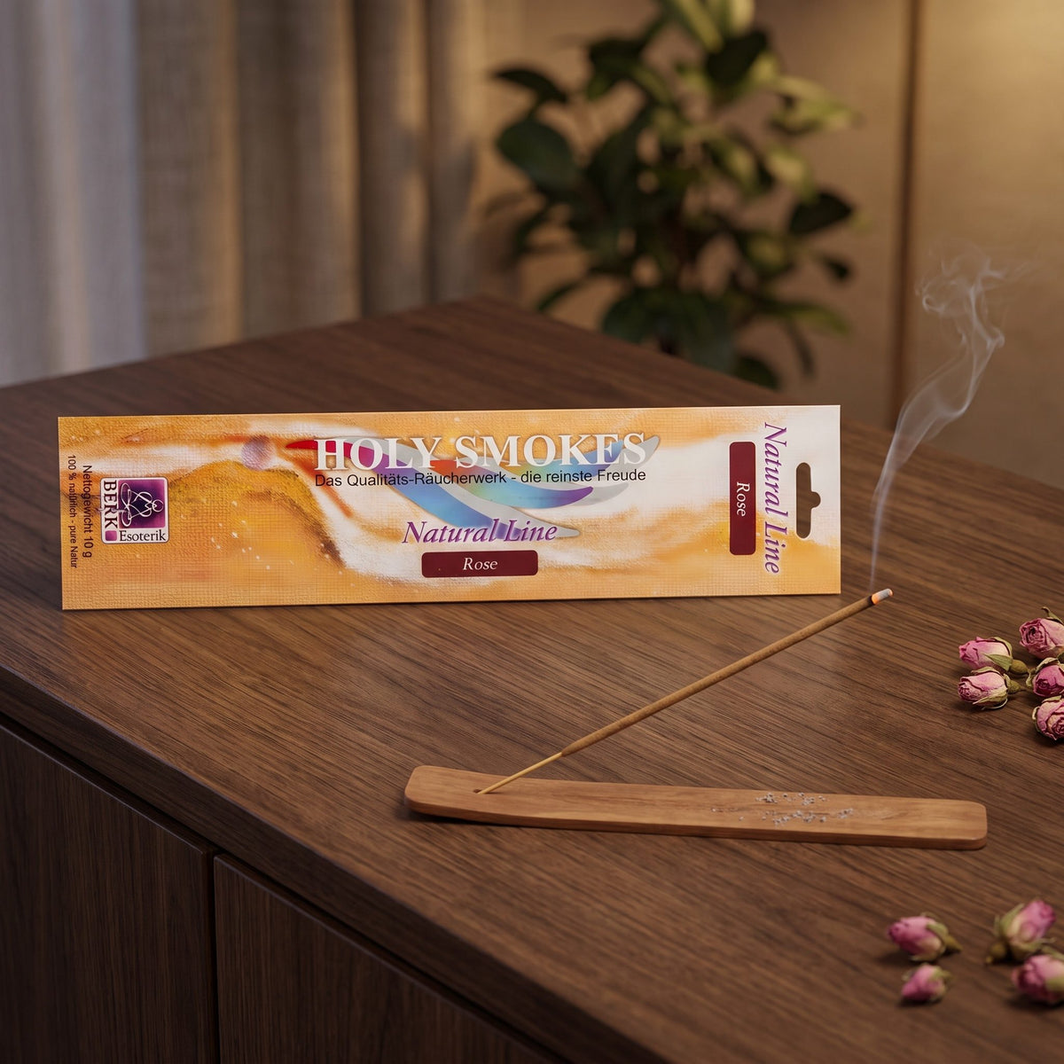 Rose Räucherstäbchen Natural Line: glimmendes Stäbchen im Holzhalter auf einem dunklen Sideboard, dahinter die Packung, am Abend