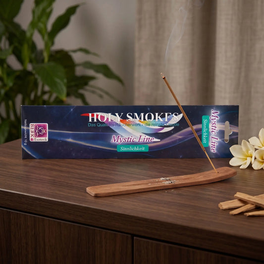 Sinnlichkeit Räucherstäbchen Holy Smokes Mystic Line: glimmendes Räucherstäbchen mit feinem Rauch im Holzhalter, dahinter die Packung, auf einem Sideboard am Abend