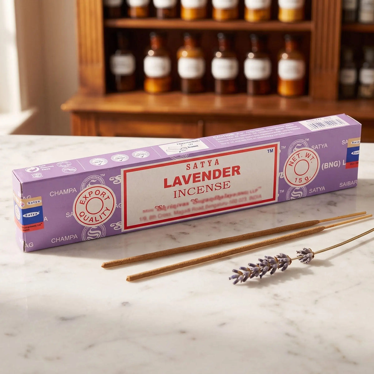 Satya Lavender Räucherstäbchen: 15-g-Packung auf einer Marmortheke vor einem Apothekerschrank, daneben zwei lose Räucherstäbchen – Spirit of Gaia