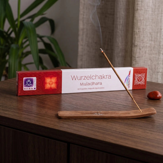 Wurzelchakra Räucherstäbchen Holy Smokes: glimmendes Räucherstäbchen mit feinem Rauch im Holzhalter, dahinter die Packung, auf einem Sideboard am Abend