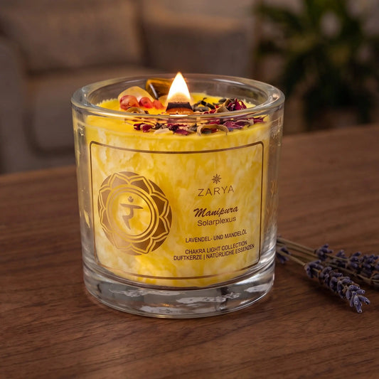 Chakra-Kerze Solarplexus Manipura mit Tigerauge, Duft Lavendel und Mandel: brennende Kerze mit kleiner Flamme am Abend auf einer dunklen Holzplatte im Wohnzimmer, daneben getrockneter Lavendel – Spirit of Gaia