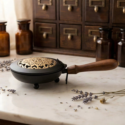 Flaches schwarzes Räuchergefäß mit goldfarbenem Mandala im Klappdeckel auf einer Marmortheke vor einem Apothekerschrank
