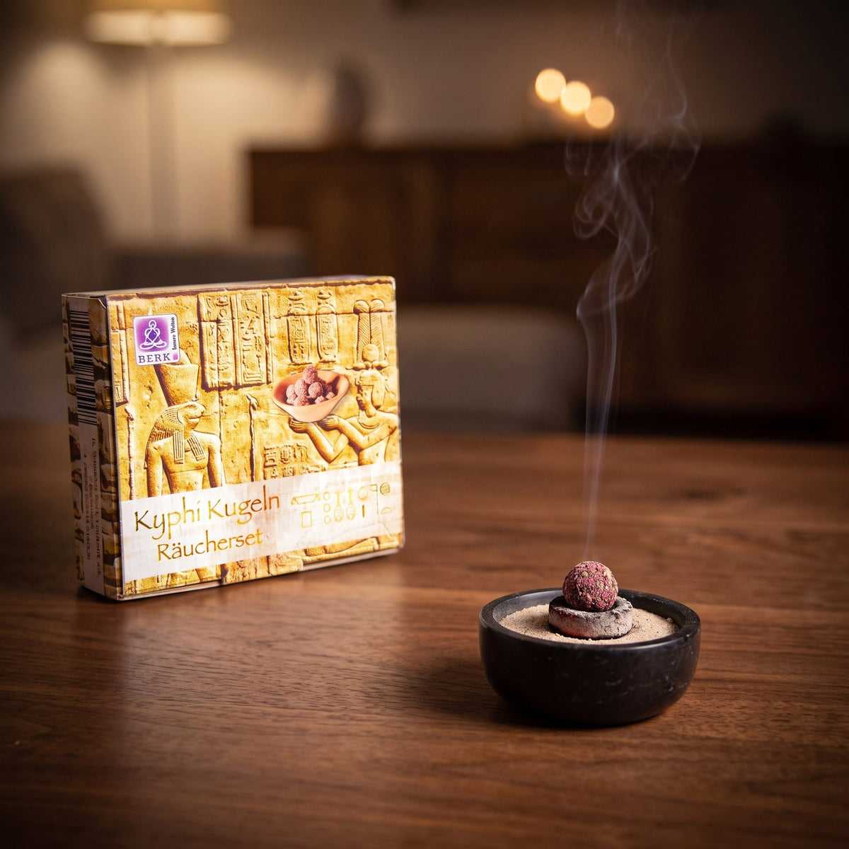 Kyphi Räucher-Set von Berk: eine Kyphi-Kugel glimmt auf der Räucherkohle in einer Specksteinschale vor der kleinen Schachtel, feiner Rauch steigt am Abend auf – Spirit of Gaia