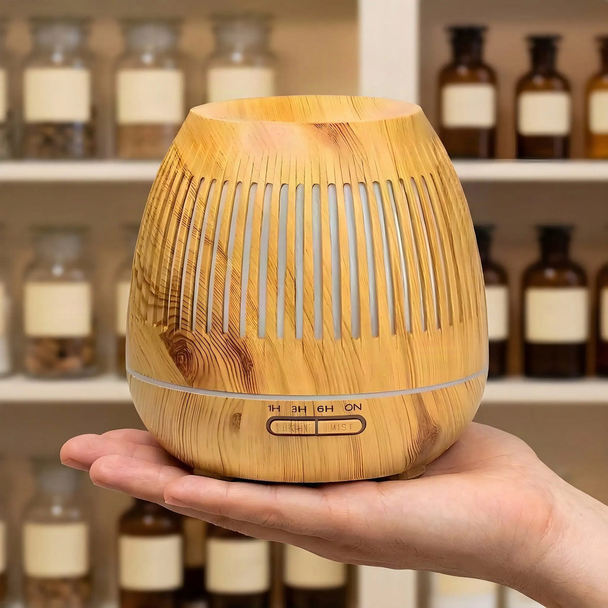Hand trägt den rund 16 cm breiten Aroma Diffuser Gaia vor einem Apothekerregal