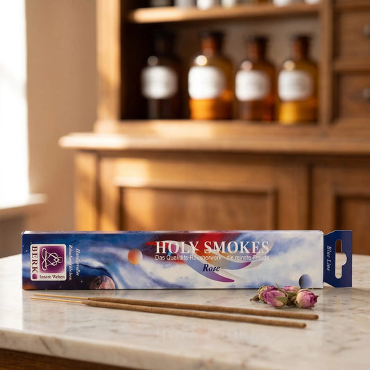 Rose Räucherstäbchen Blue Line: Packung auf einer Marmortheke vor einem Apothekerschrank, daneben zwei lose Räucherstäbchen und ein paar getrocknete Rosenknospen – Spirit of Gaia