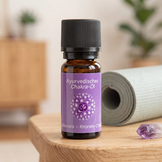Ayurvedisches Chakra-Öl Sahasrara (Kronen-Chakra): 10-ml-Fläschchen auf einem Holzhocker neben einer gerollten Yogamatte, daneben Amethyst