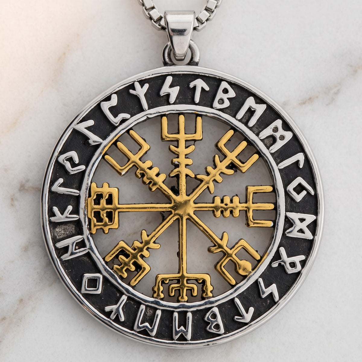 Nahaufnahme des goldfarbenen Vegvisir mit acht Armen und dem Ring aus Runenzeichen auf hellem Marmor