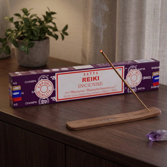 Satya Reiki Räucherstäbchen: glimmendes Räucherstäbchen mit feinem Rauch im Holzhalter, dahinter die Packung, auf einem Sideboard am Abend
