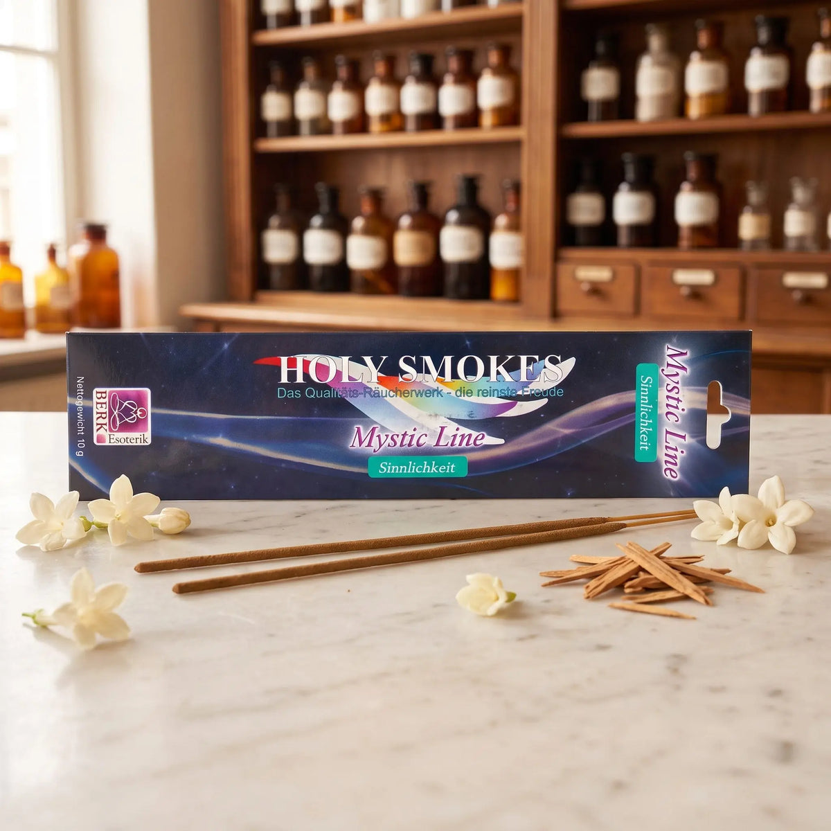 Sinnlichkeit Räucherstäbchen Holy Smokes Mystic Line: Packung auf einer Marmortheke vor einem Apothekerschrank, davor zwei lose Räucherstäbchen, weiße Blüten und Sandelholz – Spirit of Gaia