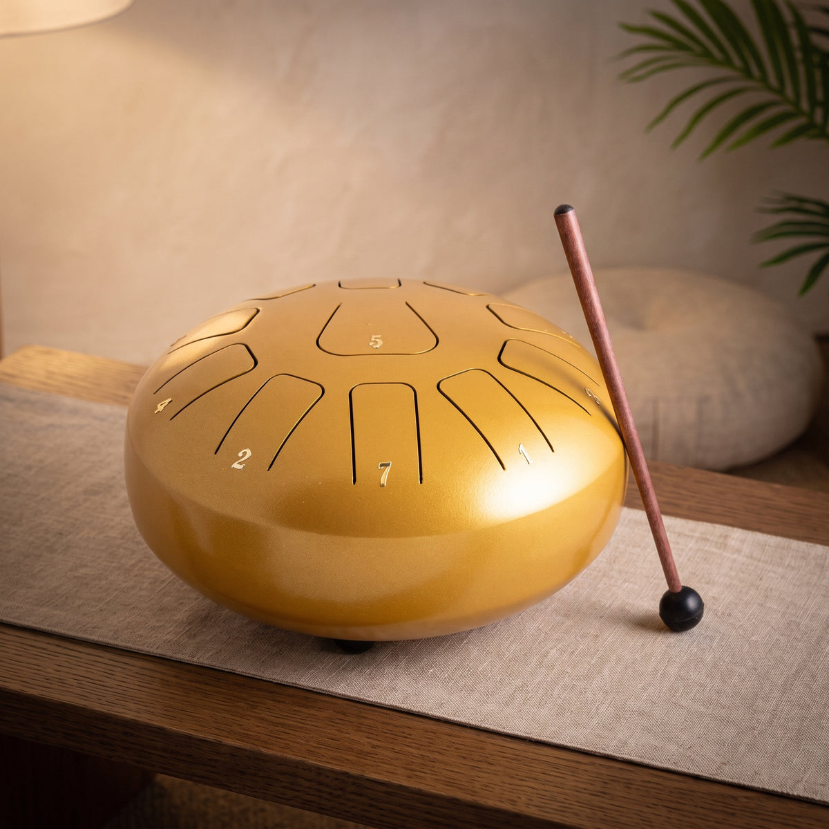Große goldene Steeldrum mit Klangstab auf einem Leinenläufer, dahinter ein warmer Meditationsraum