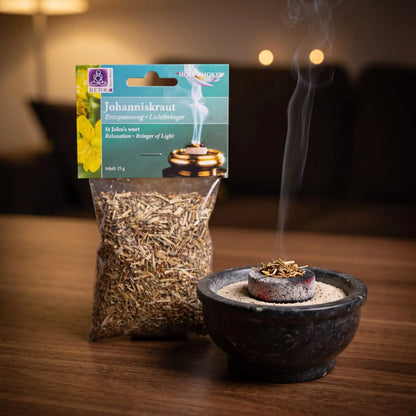 Johanniskraut, sortenreines Räucherwerk von Berk, 25 g: eine Prise Johanniskraut glimmt auf der Räucherkohle, dahinter die Tüte, feiner Rauch steigt auf einer dunklen Holzplatte am Abend auf – Spirit of Gaia