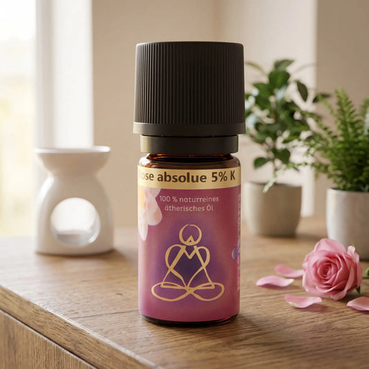 Ätherisches Öl Rose absolue: Fläschchen auf einem Holz-Sideboard im Wohnzimmer, im Hintergrund eine weiße Duftlampe, daneben eine Rosenblüte