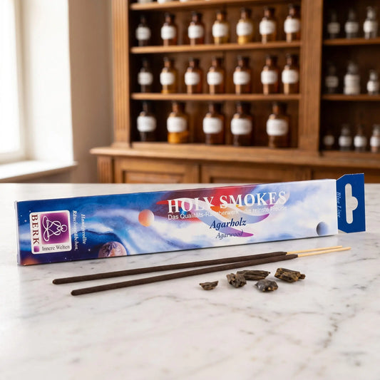 Agarholz Räucherstäbchen Holy Smokes Blue Line: Packung auf einer Marmortheke vor einem Apothekerschrank, davor zwei lose Räucherstäbchen und dunkle Agarholzstücke – Spirit of Gaia