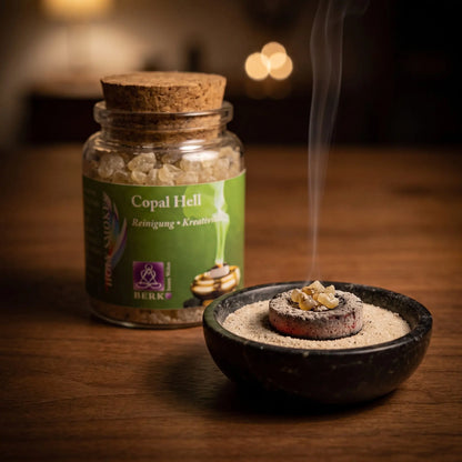 Copal Hell, reines Räucherharz von Berk, 60 ml im Korkglas: einige helle Copalstücke glimmen auf der Räucherkohle, dahinter das Korkglas, feiner Rauch steigt auf einer dunklen Holzplatte am Abend auf – Spirit of Gaia
