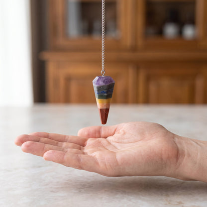 Das 7-Chakra-Pendel hängt ruhig an seiner silberfarbenen Kette über einer offenen Handfläche