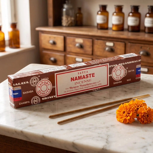 Satya Namaste Räucherstäbchen: 15-g-Packung auf einer Marmortheke vor einem Apothekerschrank, daneben zwei lose Räucherstäbchen – Spirit of Gaia