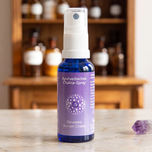 Ayurvedisches Chakra-Spray Sahasrara (Kronen-Chakra): 30-ml-Sprühflasche aus blauem Glas auf Marmortheke vor Apothekerschrank, daneben Amethyst – Spirit of Gaia