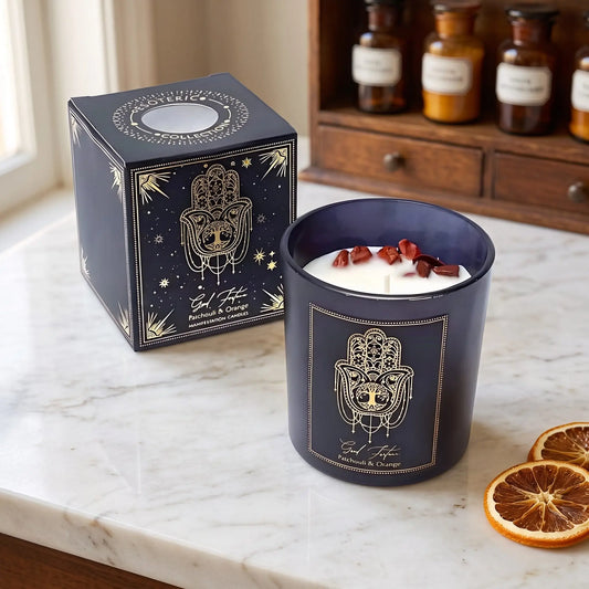 Manifestationskerze Good Fortune mit rotem Jaspis (Patchouli & Orange) von Pure Works: Kerze im schwarzen Glas und schwarze Schachtel mit Goldprägung auf Marmortheke vor Apothekerschrank, daneben getrocknete Orangenscheiben – Spirit of Gaia
