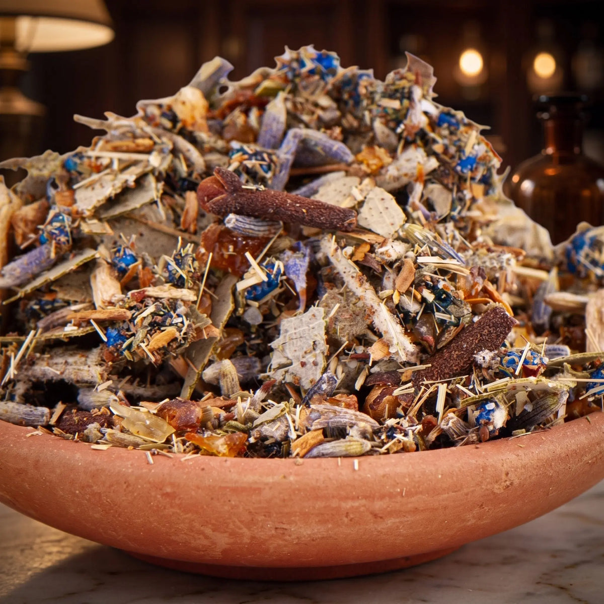Vampirschreck, Räuchermischung der Reihe Kraftvoll Räuchern von Berk, 60 ml im Bügelglas: Nahaufnahme der Terracottaschale mit Kräutern, Lavendel und blauen Blüten vor der warmen, unscharfen Abendapotheke – Spirit of Gaia