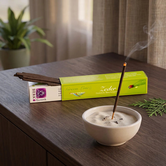 Zeder Räucherstäbchen naturrein, Holy Smokes Green Line: glimmendes Räucherstäbchen in einer Keramikschale mit Sand, dahinter die geöffnete Packung, auf einem Sideboard am Abend