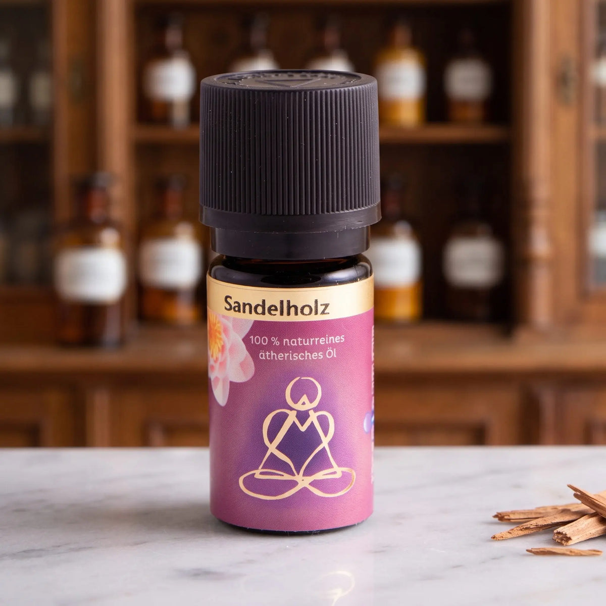 Ätherisches Öl Sandelholz: Fläschchen aus Braunglas auf Marmortheke vor Apothekerschrank, daneben Sandelholzspäne – Spirit of Gaia