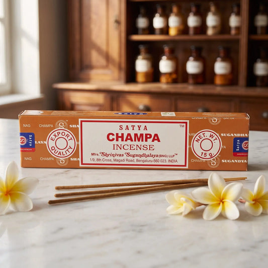 Satya Champa Räucherstäbchen: 15-g-Packung auf einer Marmortheke vor einem Apothekerschrank, daneben zwei lose Räucherstäbchen – Spirit of Gaia