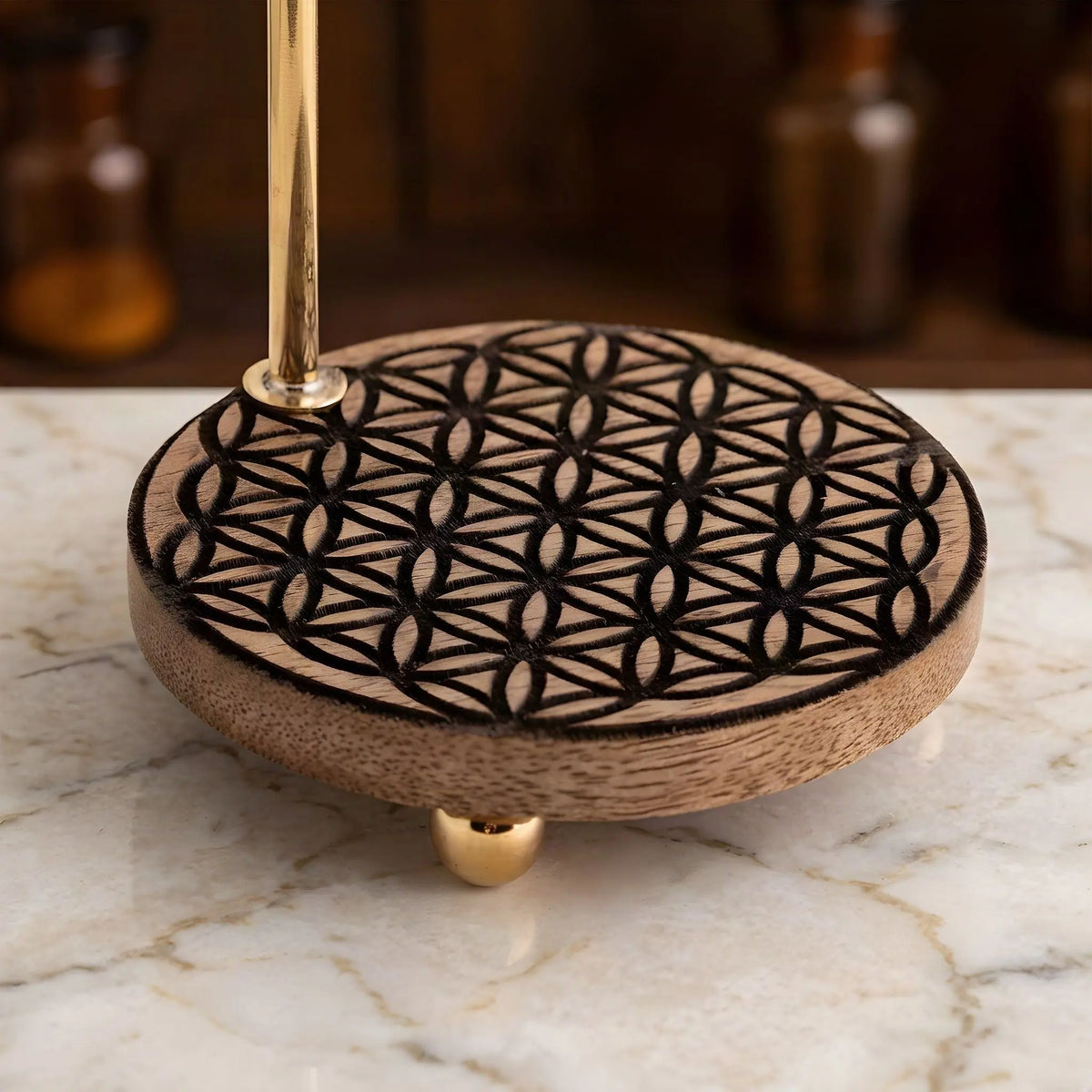 Die in den Mangoholzsockel gebrannte Blume des Lebens aus der Nähe, dahinter unscharf der Apothekerschrank