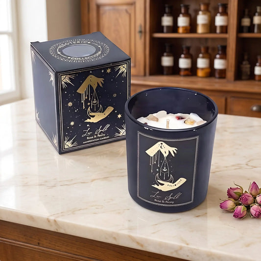 Manifestationskerze Love Spell mit Rosenquarz (Rose & Pfingstrose) von Pure Works: Kerze im schwarzen Glas und schwarze Schachtel mit Goldprägung auf Marmortheke vor Apothekerschrank, daneben getrocknete Rosenknospen – Spirit of Gaia