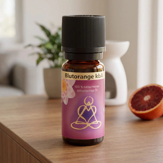 Ätherisches Öl Blutorange: Fläschchen auf einem Holz-Sideboard im Wohnzimmer, im Hintergrund eine weiße Duftlampe, daneben eine halbierte Blutorange