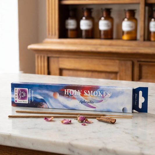 Aphrodite Räucherstäbchen Blue Line: Packung auf einer Marmortheke vor einem Apothekerschrank, daneben zwei lose Räucherstäbchen und ein paar Rosenblätter und ein Stück Zimtrinde – Spirit of Gaia