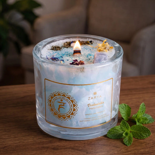 Chakra-Kerze Halschakra Vishuddha mit Aquamarin und Calcit, Duft Minze und Mandel: brennende Kerze mit kleiner Flamme am Abend auf einer dunklen Holzplatte im Wohnzimmer, daneben frische Minze – Spirit of Gaia
